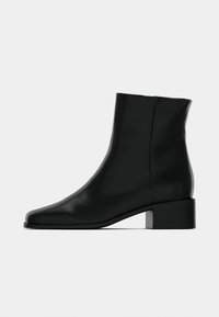 Bottines noires en cuir lisse avec un bout carré, un talon bas en bloc, et un détail de couture minimaliste sur les côtés.