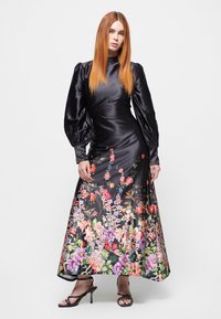 Sort satin kjole med lange pufærmer, der har et blomstermotiv i klare farver ved kanten. Båret med strappy sorte hæle.