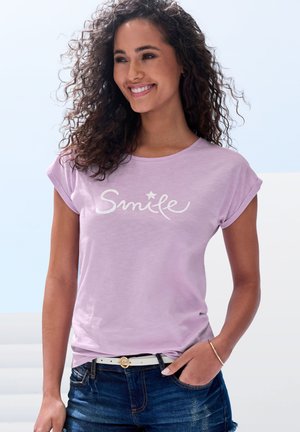 Short-sleeve lavender T-shirt with "Smile" text in white, round neckline, soft fabric, paired with dark denim shorts and a white belt.