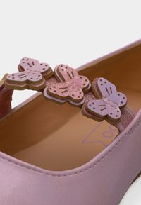 Ballerine rose avec une finition satinée lisse. Dotée d'une bride ornée de trois appliqués papillons superposés en rose et violet.