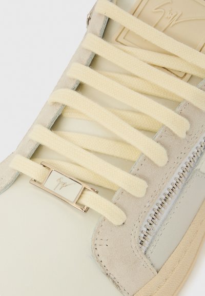 Baskets de couleur claire présentant un mélange de cuir et de daim, des lacets plats jaunes, un détail logo en métal et une fermeture éclair latérale.