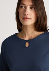Navy blue top with a rounded neckline featuring a keyhole cutout. Made of soft fabric with a smooth texture and long sleeves.