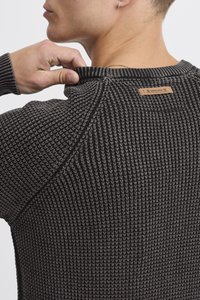 Striktrøje i mørkegrå med tekstureret stof, ribbede manchetter og et lædermærke i nakken. Rund halsudskæring og tætsiddende design.