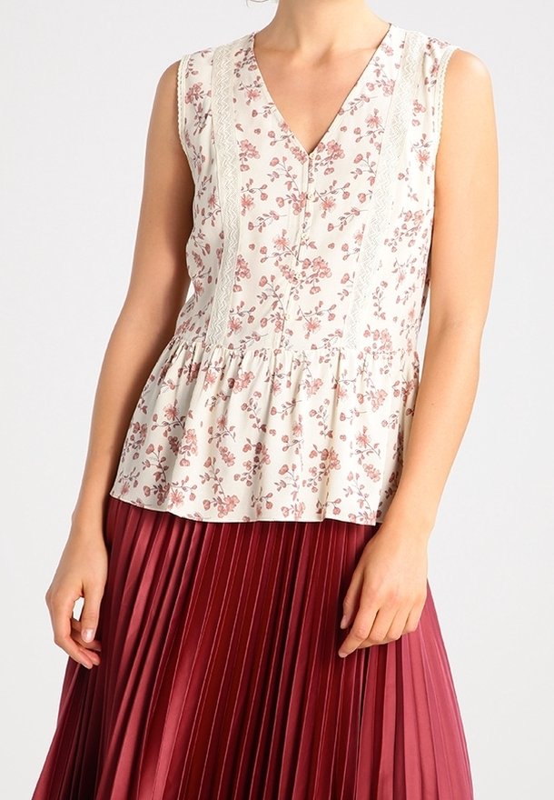 Ärmellose Bluse aus cremefarbener Baumwolle mit pinken Blumenmustern und Spitzenabschlüssen, kombiniert mit einem plissierten burgunderfarbenen Rock.
