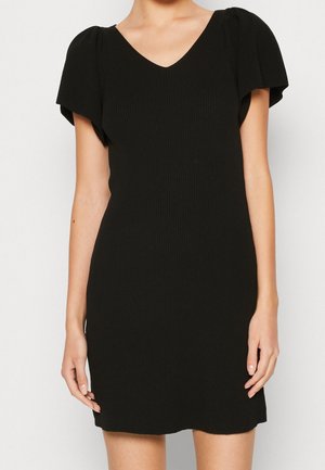 Czarna sukienka z krótkim rękawem, bufkami przy rękawach i dekoltem w serek, sięgająca do połowy uda, na stojącej osobie na jednolitym tle.