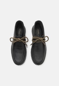 Chaussures en cuir noir à bouts ronds, avec des lacets bruns contrastants, des semelles en caoutchouc texturé et une finition lisse. Logo Clarks sur les semelles intérieures.