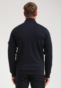 Sweat-shirt bleu marine, col rond, manches longues, design ajusté, avec une poche utility sur la manche gauche, texture de tissu douce.
