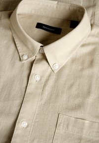 Beige linen shirt with a button-down collar, white buttons, and a chest pocket; smooth texture with a subtle, natural weave pattern.