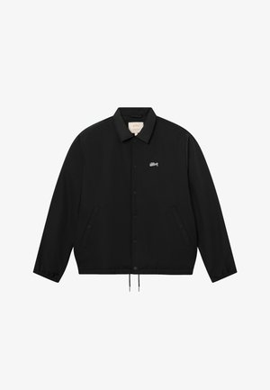 Black button-up jacket with collar, elastic cuffs, two front pockets, and small white script logo on the left chest.