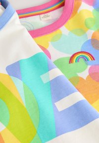 Maglietta colorata con motivi geometrici multicolori, colli a costine azzurro chiaro e rosa, e un dettaglio ricamato con un arcobaleno.