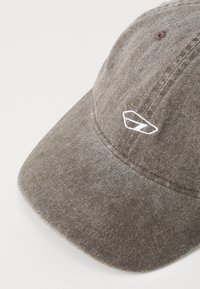 Brown cotton cap with a curved brim, featuring white embroidered logo and visible stitching details on the fabric.