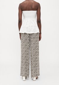 Haut peplum sans manches en coton blanc avec un motif texturé ; associé à un pantalon large à motifs en diamants marron et blanc et des sandales à talons blanches.