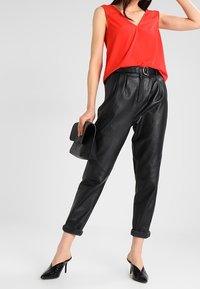 Rød ærmeløs top med V-udskæring og blonder, parret med løse sorte læderbukser, prydet med opkrøllede manchetter og et sort bælte.