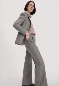 Grijze op maat gemaakte pak met wijde broekspijpen en een getailleerde blazer, gecombineerd met een zachtroze coltrui. Glad stof met subtiele textuurdetails.