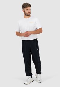 Biele bavlnené tričko s krátkymi rukávmi a zlatým logom, v kombinácii s čiernymi športovými nohavicami s elastickým pásom a potlačeným logom.