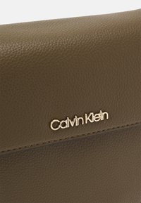 Brązowa skórzana kopertówka o teksturowanej powierzchni z złotym logo Calvin Klein. Posiada gładkie wykończenie i subtelne detale podszycia wzdłuż krawędzi.