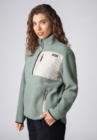  Lichtgroene fleecejack met een crèmekleurig paneel, ritssluiting op de borst en zijzakken. Voorzien van een hoge kraag en marineblauwe accenten bij de manchet.