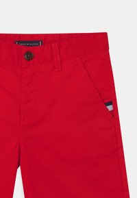 Rote Tommy Hilfiger-Hosen mit Knopfverschluss, Gürtelschlaufen, schrägem Fronttasche und einem kleinen Flaggenmotiv in der Tasche.