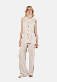 Blazer sans manches rayé beige clair avec revers crantés, fermeture à trois boutons et poches avant, associé à un pantalon large assorti.