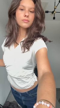 Top blanco de manga corta con laterales fruncidos, combinado con jeans azules. La tela parece suave con una textura lisa.