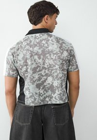 Koszulka polo z krótkim rękawem, z czarnym kołnierzykiem, szarym wzorem w kamuflaż oraz jednolitymi czarnymi panelami bocznymi, w luźnym kroju.