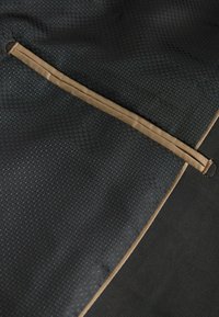 Schwarzer, hexagonal gemusterter Stoff mit matter Oberfläche, versehen mit einem beigen Riemen, der an der Ecke befestigt ist und den Kontrast in der Textur hervorhebt.