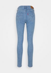 Jean en denim bleu clair, coupe slim, affiché de dos, avec deux poches arrière et un patch logo en cuir marron sur la ceinture.