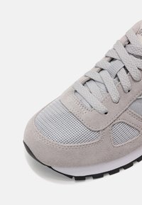 Gros plan de l'avant d'une basket gris clair avec dessus en daim et mesh, lacets épais texturés et semelle en caoutchouc noire et blanche.