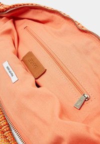 Perzikkleurig interieur van een tas met een ritsvak, leren etiket en een textielvoering. Voorzien van een gevlochten randontwerp.