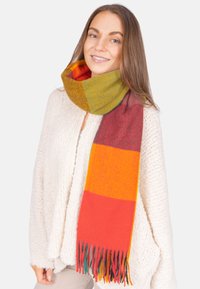 Mehrfarbiger Schal mit Streifen in Grün, Orange, Rot und Gelb, aus weicher Wolle mit fransigen Enden. Um den Hals gewickelt getragen.