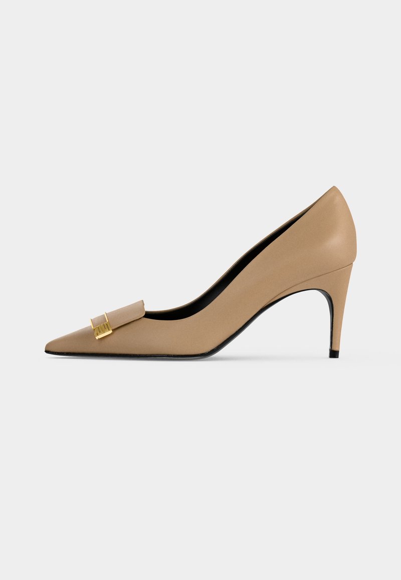 Beige leather high-heeled shoe with pointed toe and decorative gold buckle on the front, shown from the side on a white background.