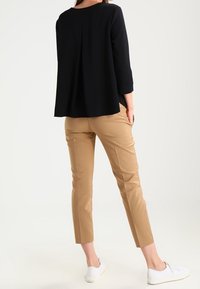 Schwarzes, locker sitzendes Langarmshirt mit einem Faltenwurf auf der Rückseite, kombiniert mit hellbraunen, engen Hosen und weißen Sneakers.