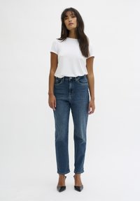 T-shirt bianco a maniche corte abbinato a jeans blu a vita alta. I jeans presentano un taglio dritto e leggeri strappi all'orlo.