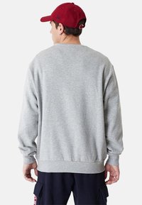 Sudadera gris de manga larga, con puños acanalados y dobladillo ajustado. Llevada al revés, mostrando una textura simple y lisa.