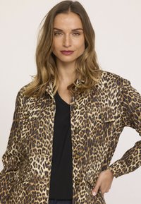 Veste en denim à imprimé léopard, dotée d'un front à boutons, de deux poches poitrine et d'une coupe décontractée. Associée à un haut noir en dessous.