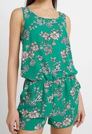 Ærmeløs grøn blomsterdragt med lyserøde og hvide blomster, elastisk talje og lommer, båret af en person stående mod en hvid baggrund.