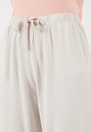 Heledad beežid lahtised püksid elastse vöökoha ja sõlmitava paelaga, kantud roosa topiga.