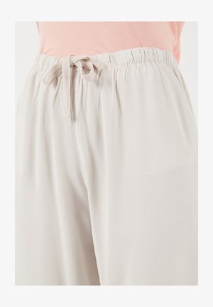 Heledad beežid lahtised püksid elastse vöökoha ja sõlmitava paelaga, kantud roosa topiga.