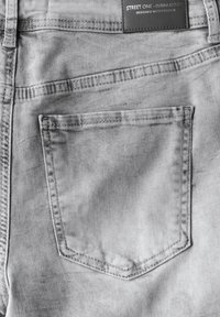 Grijze denim jeans met een enkele achterzak. Eigenschappen zijn een gestikt ontwerp, een versleten textuur en een rechthoekig etiket op de tailleband.
