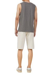 Grijze mouwloze top met een relaxte pasvorm, gecombineerd met crèmekleurige knielange shorts en lichtkleurige sneakers met grijze accenten.