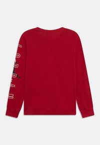 Red long-sleeve t-shirt featuring white text and a black silhouette on one sleeve, with a round neck and a soft texture.