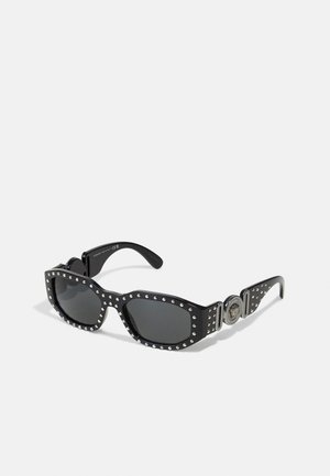 Lunettes de soleil noires avec des verres rectangulaires, des accents cloutés autour de la monture, et un détail en matériel circulaire sur les branches. La texture est lisse.
