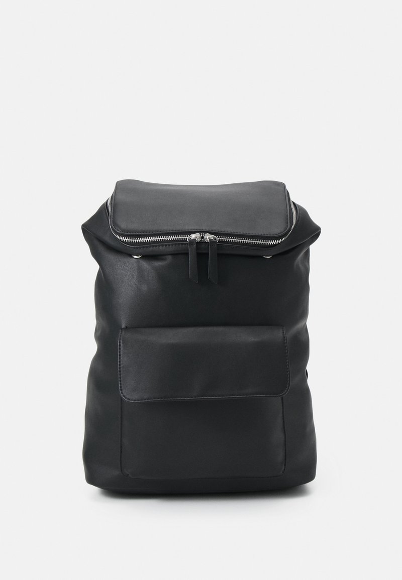 Sac à dos en cuir noir avec une fermeture éclair sur le dessus, une forme carrée, une poche avant et une texture lisse. Il présente une quincaillerie argentée et un design minimaliste.