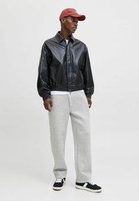 Geacă din piele neagră tip bomber, cu manșete elastice, pantaloni de trening gri și sneakers negri cu accente albe. O șapcă roșie adaugă un contrast de culoare.