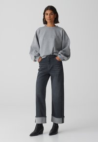 Felpa grigia oversize con scollatura a coste, abbinata a jeans scuri a vita alta con risvolti e stivaletti neri a punta.