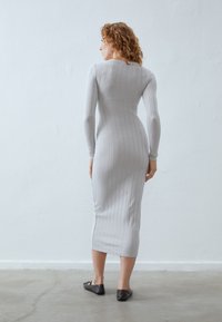 Gray ribbed knit dress with long sleeves, fitted shape, and knee-length. Worn with dark flats, against a light textured background.