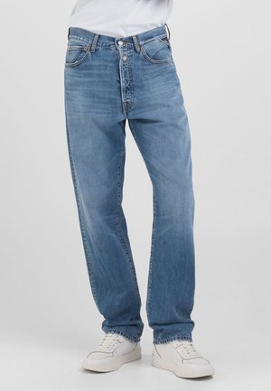 Vaqueros de mezclilla azul claro con un corte holgado, que cuentan con una bragueta de botones, un diseño de cinco bolsillos y un ligero desvanecimiento. Combinados con zapatillas blancas.