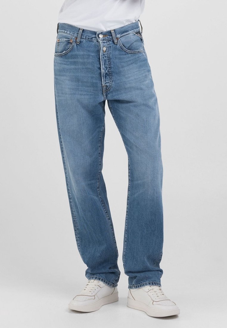 Vaqueros de mezclilla azul claro con un corte holgado, que cuentan con una bragueta de botones, un diseño de cinco bolsillos y un ligero desvanecimiento. Combinados con zapatillas blancas.