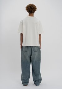 Λευκή βαμβακερή μπλούζα με κοντά μανίκια, συνδυασμένη με φαρδιά μπλε τζιν παντελόνια με ξεθωριασμένο φινίρισμα και πίσω τσέπες.