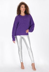 Paars wollen sweater met juweelaccenten op de halslijn, gecombineerd met getailleerde zilverkleurige metallic leggings en sandalen met bandjes.